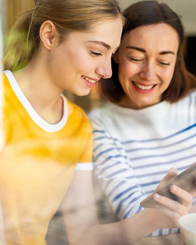 Mother in striped shirt and daughter in yellow shirt looking at a smartphone