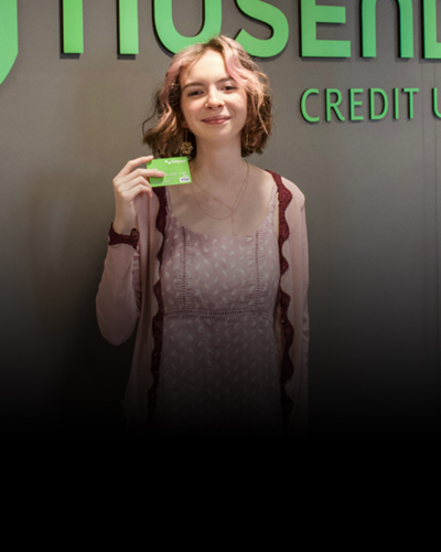 Young person at a Nusenda Credit Union branch holding a debit card.